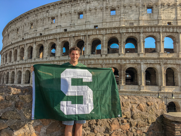 AFRE undergrad student holding Spartan flag in front of the Colosseum