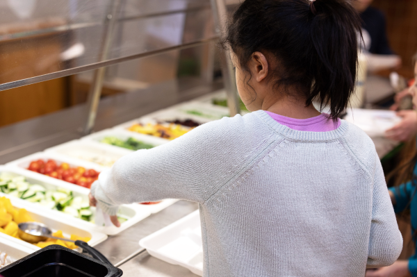 Young girl serves herself fresh sliced cucumbers from a salad bar