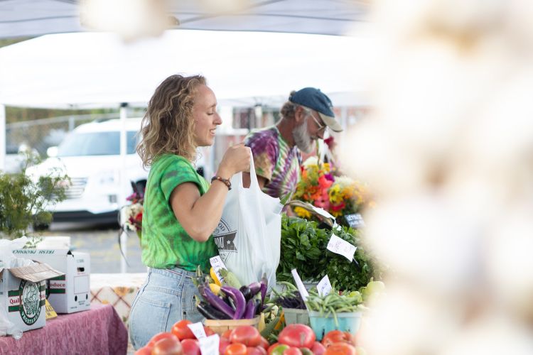 Woman hands a bag of produce over the stall at a farmers market