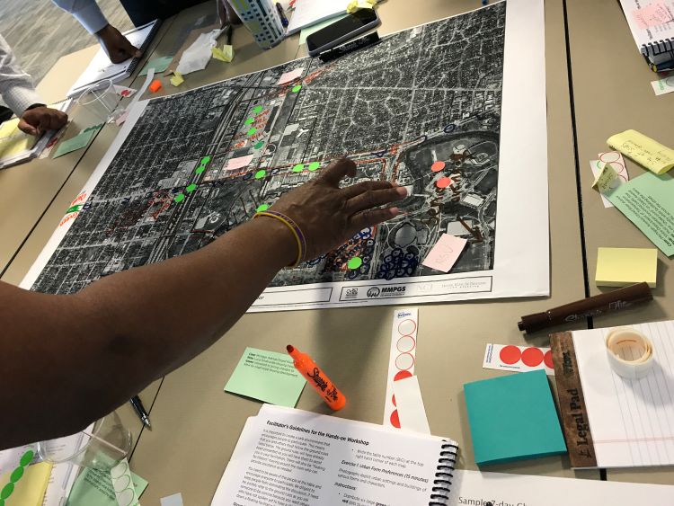 Hand placing dots on a neighborhood plan during group work at an NCI charrette training session.