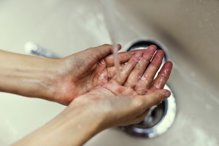 Hands under running water in sink.