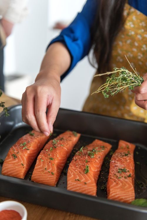 Salmon with rosemary being prepared by a woman in an apron.