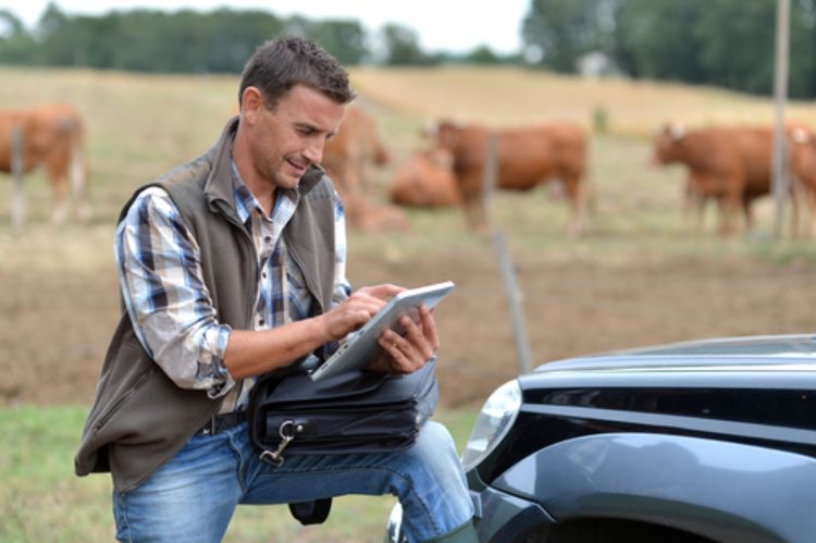 A young farmer looking at a tablet with a field in the background.
