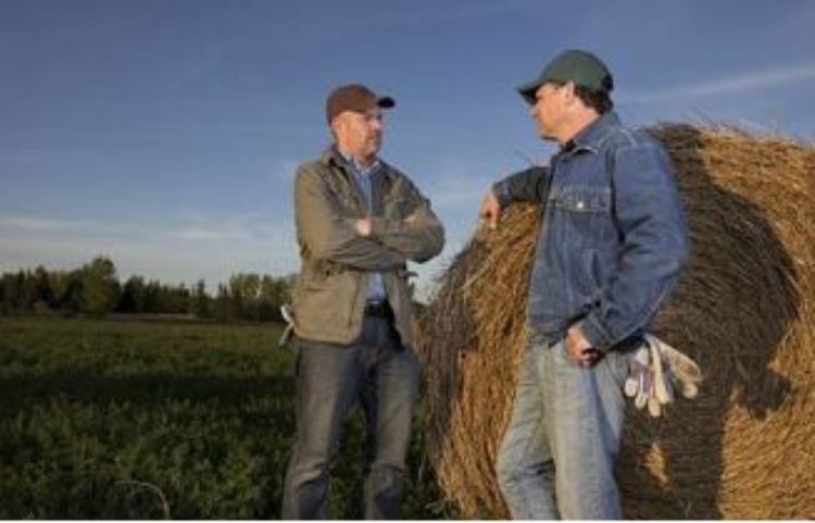 Two men standing near a bail of hay.