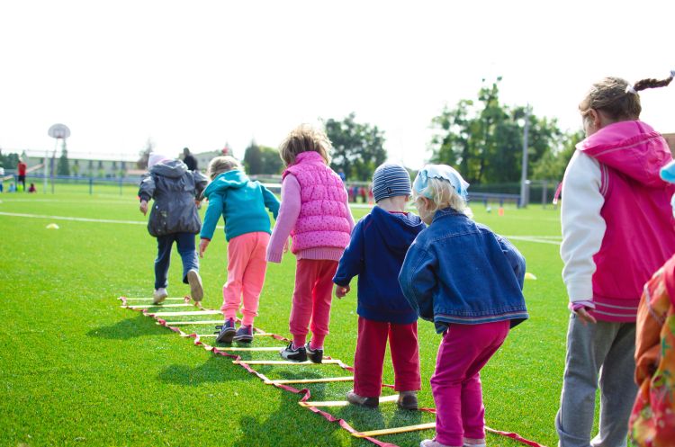 Children in a row hopping over a ladder on a field.