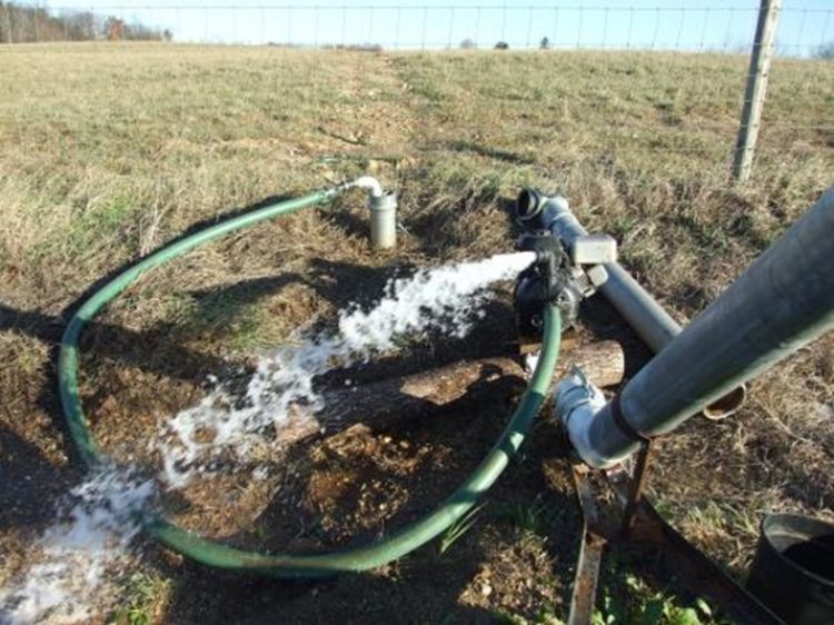 A water pump in a field pouring water out of it.
