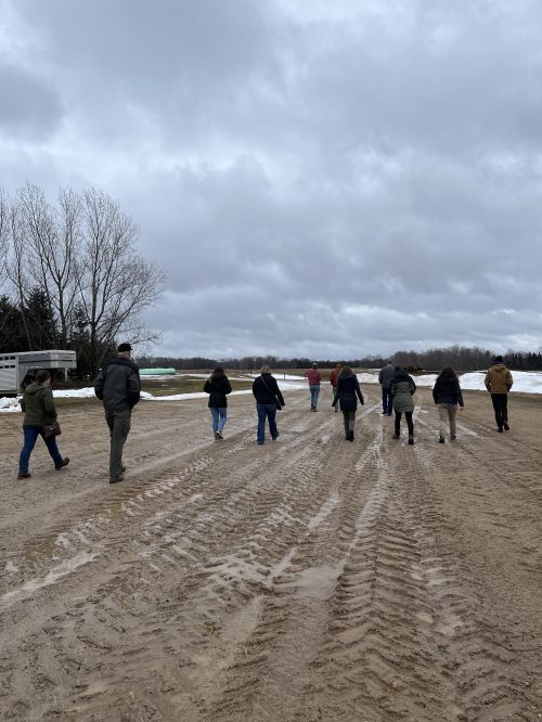 A group of people walking on a muddy road towards a snow-covered field.