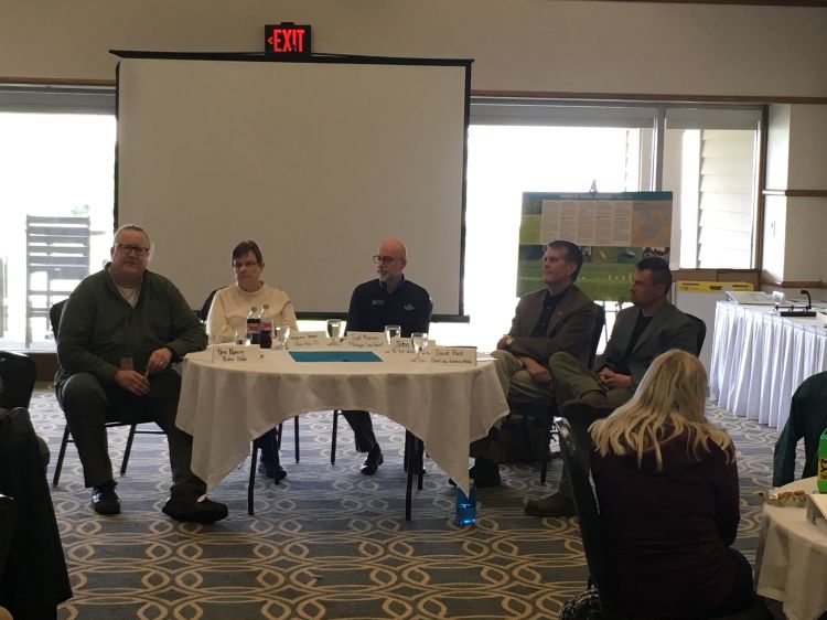 Five people representing science communicators sit around half of a round table facing a group as part of a discussion panel on science communication.