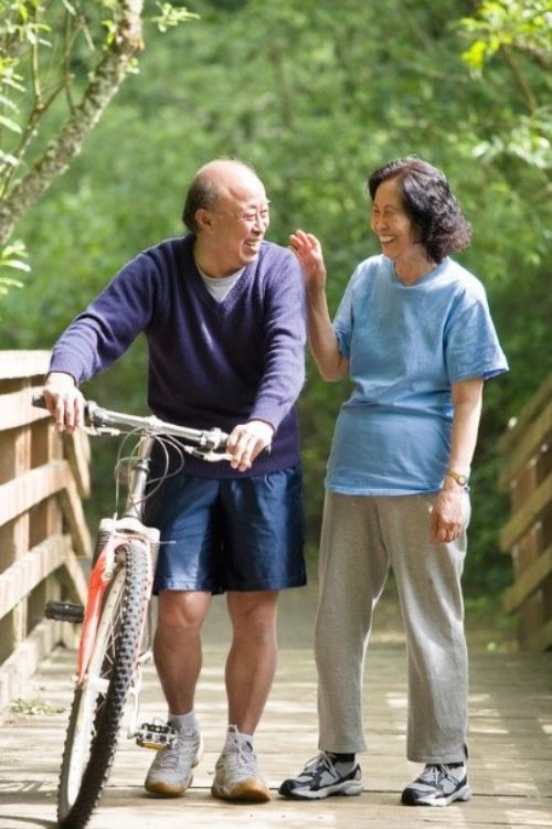 An older couple smiling while walking a bicycle over a bridge.