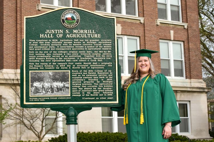 Michigan State University student Lauren Heberling outside of Morrill Hall of Agriculture on campus in her graduation cap and gown.