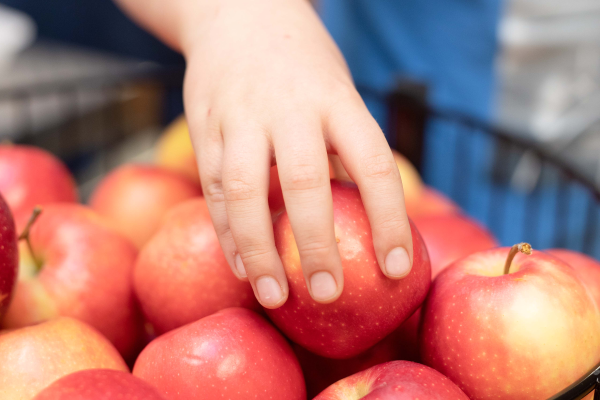 Child's hand reaches for a fresh apple in a bowl