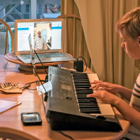 Girl playing the piano with laptop open in next to her