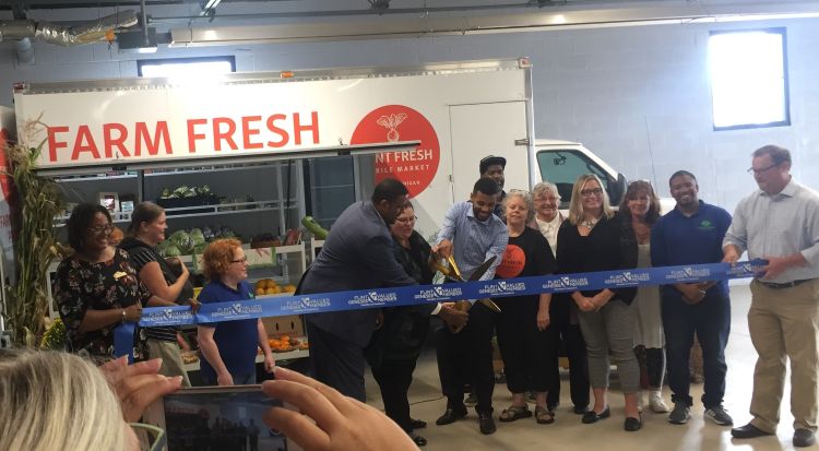 The ribbon cutting image has numerous staff and organizational partners of the Flint Fresh Food Hub.