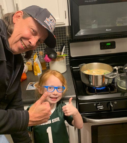 Man and girl give thumbs up next to soup pot on stove