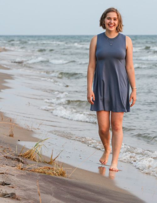 Teenager Emeline Hanna walks barefoot along a lakefront in the sand with small waves rolling up on the sand.