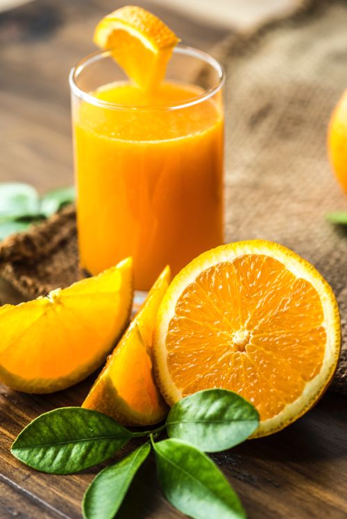 Glass of orange juice surrounded by sliced oranges.