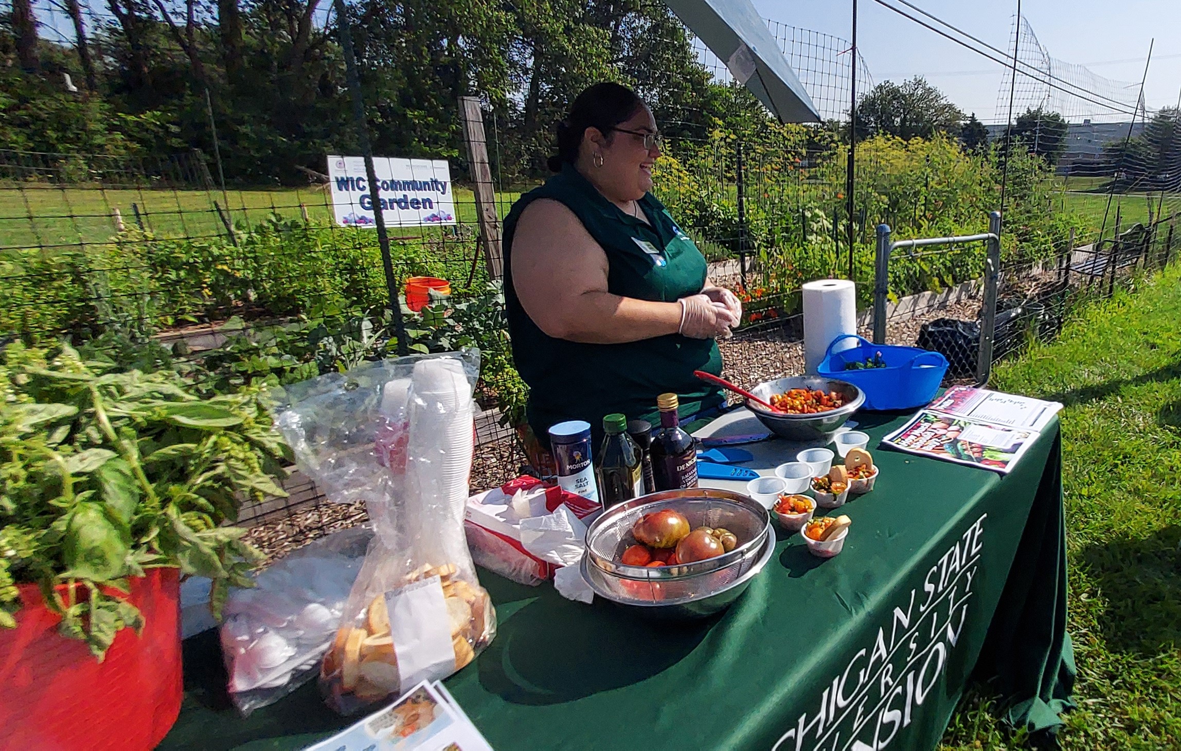 A woman stands at a table surrounded by produce and ingredients.