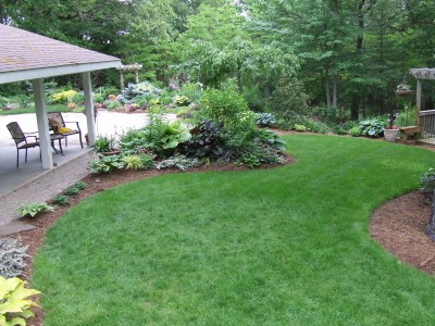 A backyard with a patio, flowers, and a well-manicured lawn.