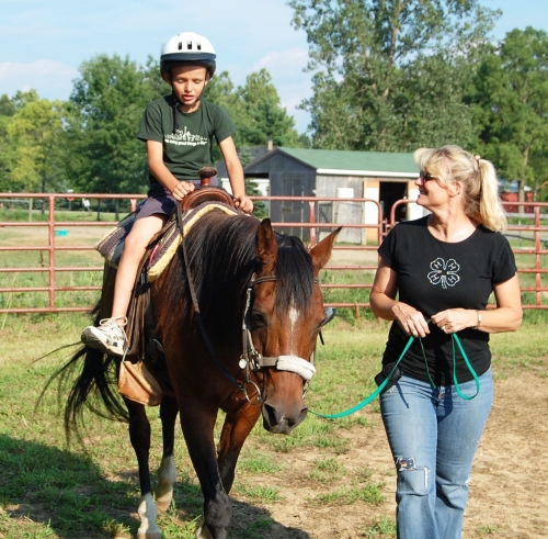 Extension Specialist walks with young boy on horse as part of therapy