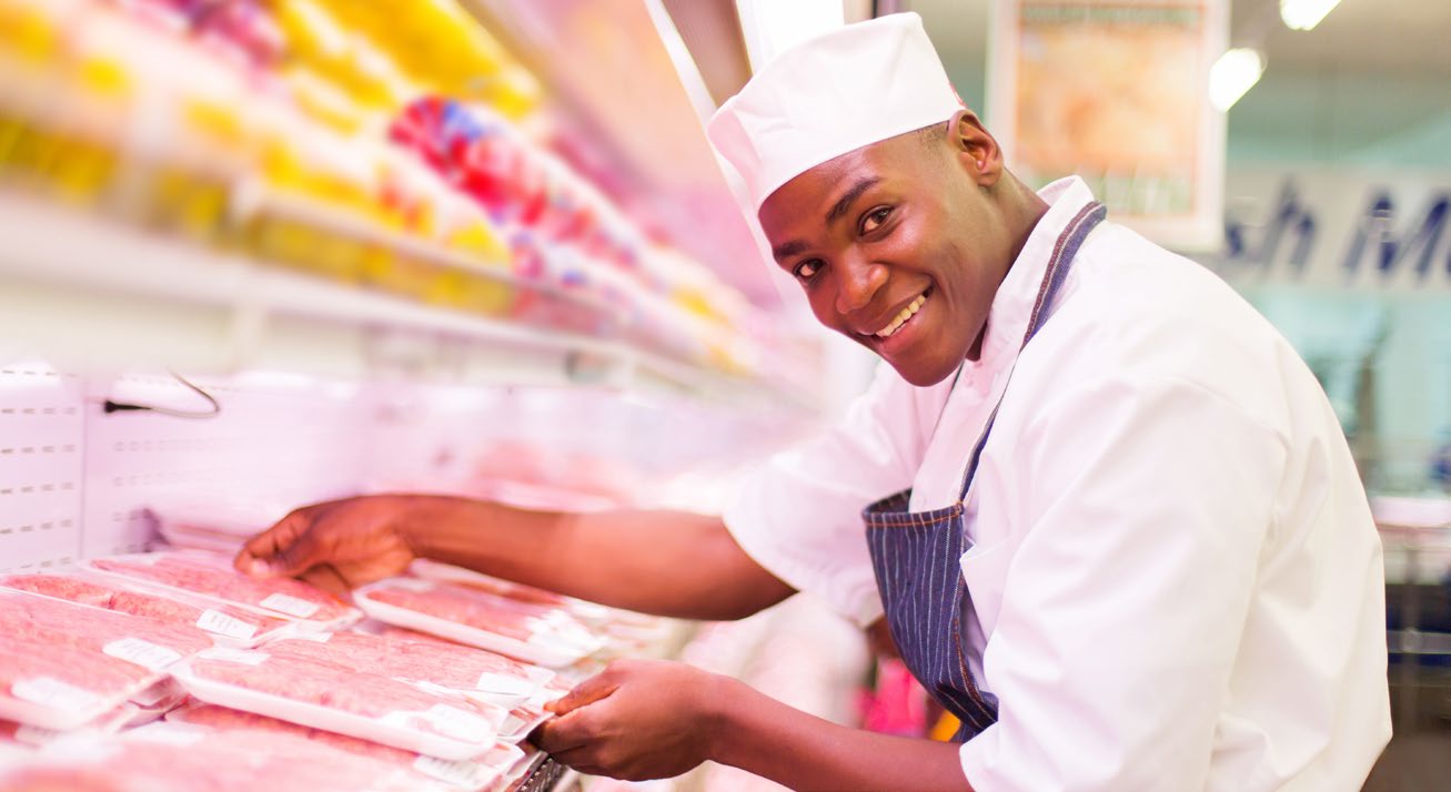 Butcher placing packaged meat on grocery store shelf.