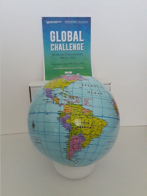 Image depicts a globe beach ball and the 2023 World Food Prize Michigan Youth Institute Global Challenge Guide.
