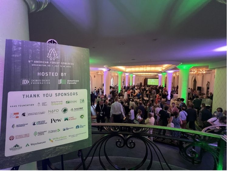 A conference room full of people gathered with a 'thank you to our sponsors' board to the on the left.