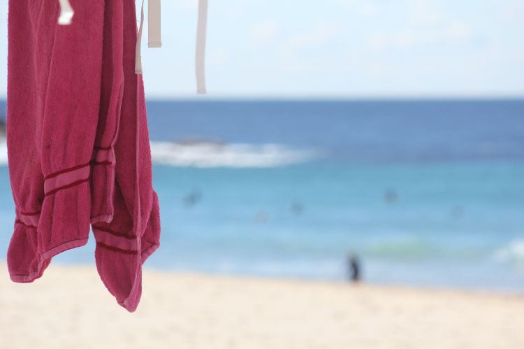 Red beach towel hanging in foreground with sandy beach and water out of focus in the background. For decorative purposes.