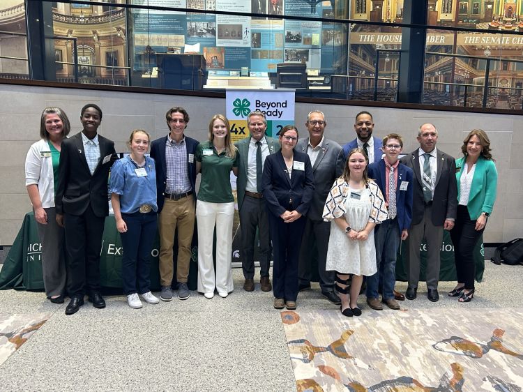 A diverse group of youth and adults in front of a 4-H sign.