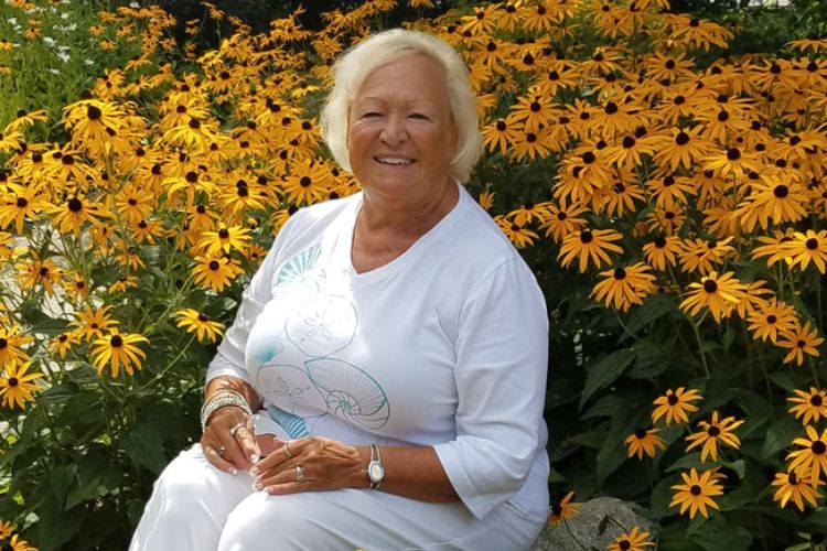 Pam Babbitt sitting on a rock in a garden of Black-eyed Susan flowers.