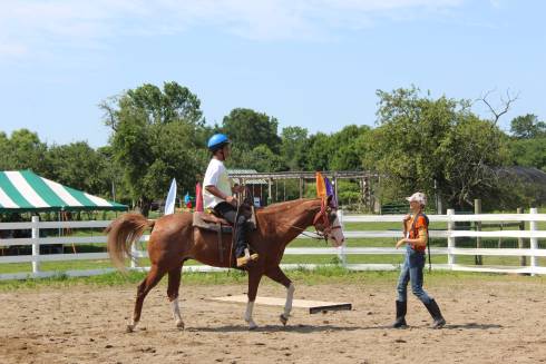 Camper riding on a horse with a horse camp instructor leading.