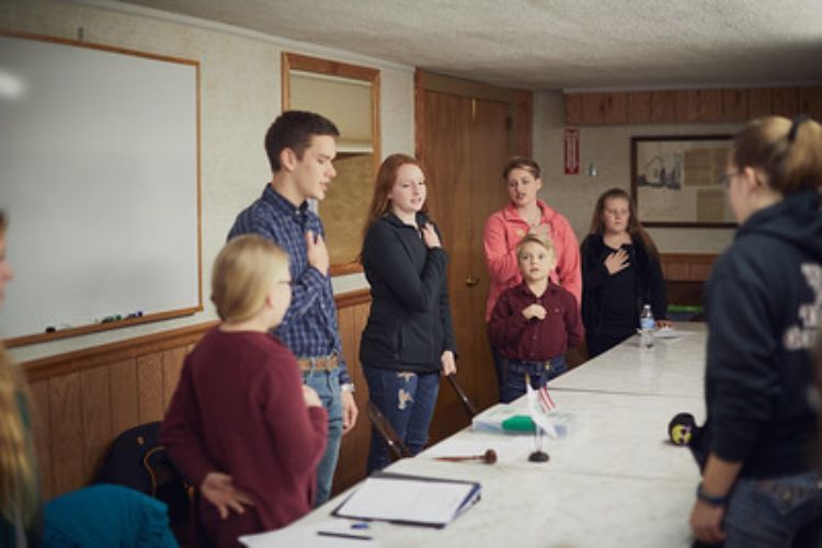 4-H club members hold their hands over their heart as they are saying the pledge at a 4-H club meeting.  Courtesy of: National 4-H Council