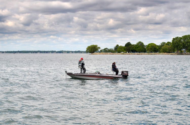 Two people are fishing from a motor boat out in a lake.