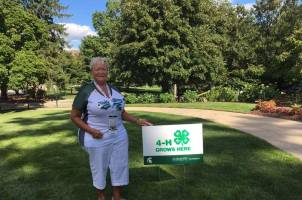Pam Babbitt, Muskegon County 4-H volunteer and Michigan 4-H Foundation trustee in front of a 4-H Grows Here yard sign.