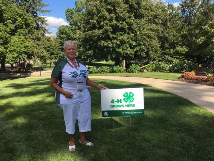 Pam Babbitt, Muskegon County 4-H volunteer and Michigan 4-H Foundation trustee in front of a 4-H Grows Here yard sign.