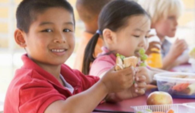 A little boy smiling at the camera before taking a bite of his sandwich