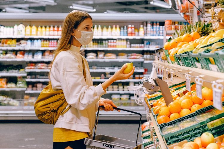 A woman look at fruit in the produce section of a grocery store.