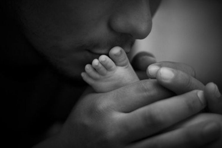 A man kissing a baby's foot.