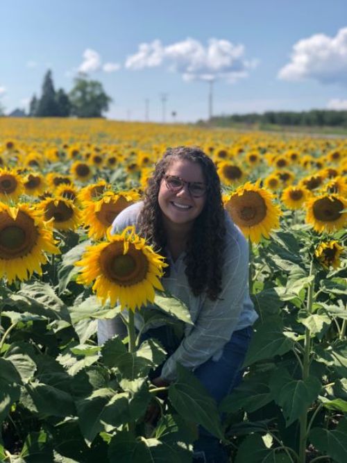 A woman sits in the middle of a field of sunflowers.