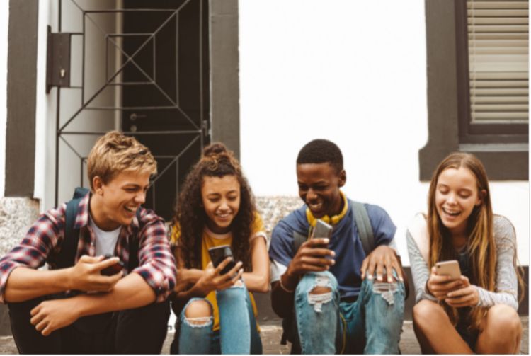A group of youth sitting on the stairs looking at their cell phones.