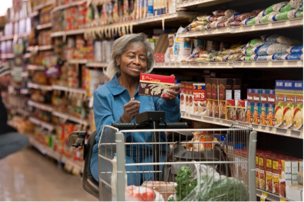 An older adult woman in a grocery store looking at the nutrition facts label on the back of a food item.
