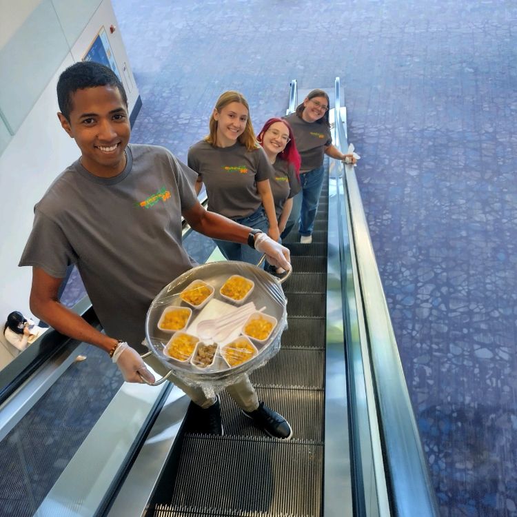 The MSU Product Development team rides an upward escalator while holding their product, Chik'n Cheese
