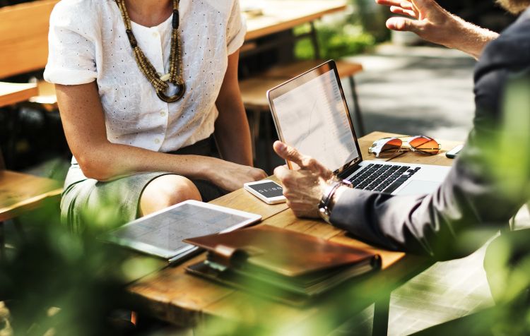 A man and women sitting talking about business, with a laptop in between them