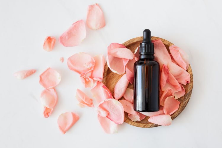 A bottle of essential oils surrounded by rose petals.