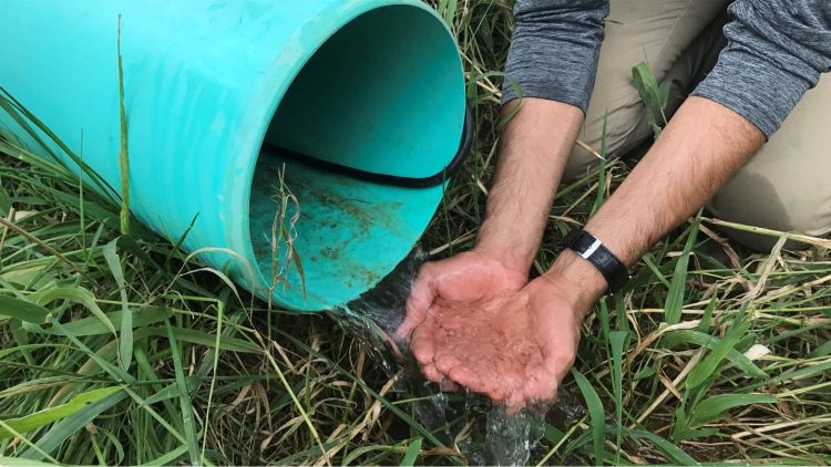 Hands catch water coming out of a drainage pipe.