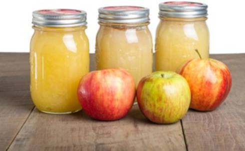 3 apple in on a counter and 3 cans of applesauce.