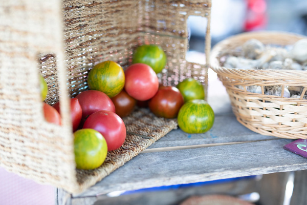 Green and red cherry tomatoes sit in a wicker basket next to a basket of garlic at a farmers market stand. Photo Credit: Khalid Ibrahim