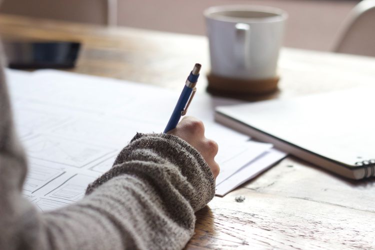 A hand holding a pen, writing on paper.