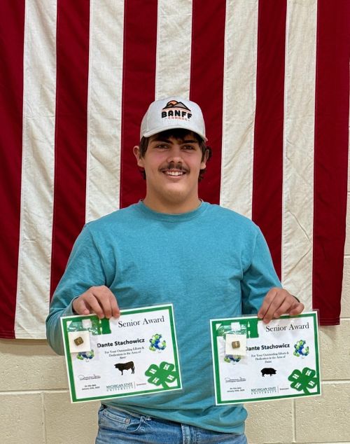 A young man holding up two certificates in front of a U.S. flag.