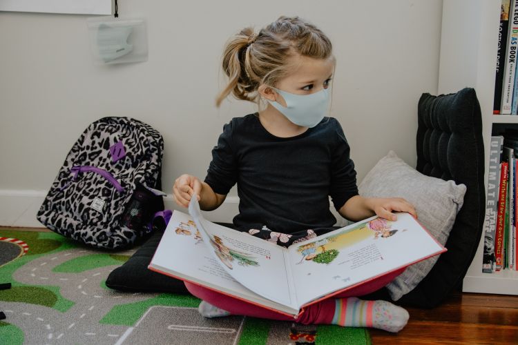 Child reading a book while wearing a mask