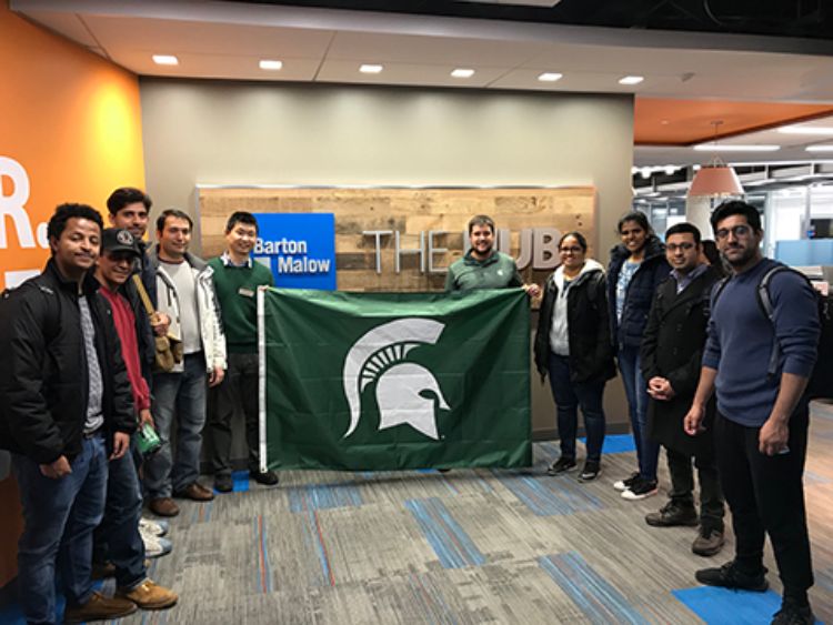 Image of students from the SPDC Construction Management Program and College of Engineering's Civil Engineering Program holding an MSU Spartan flag in Barton Malow.